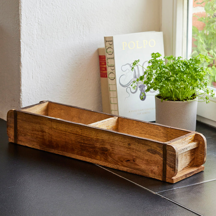 Boîte en bois à trois compartiments sur un comptoir de cuisine, à côté un livre de cuisine et un pot d'herbes fraîches.