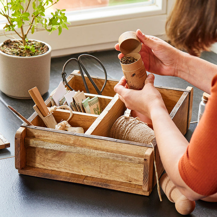 Personne remplissant de la terre dans un pot de fleurs biodégradable au-dessus d'une boîte en bois avec des accessoires de jardinage"