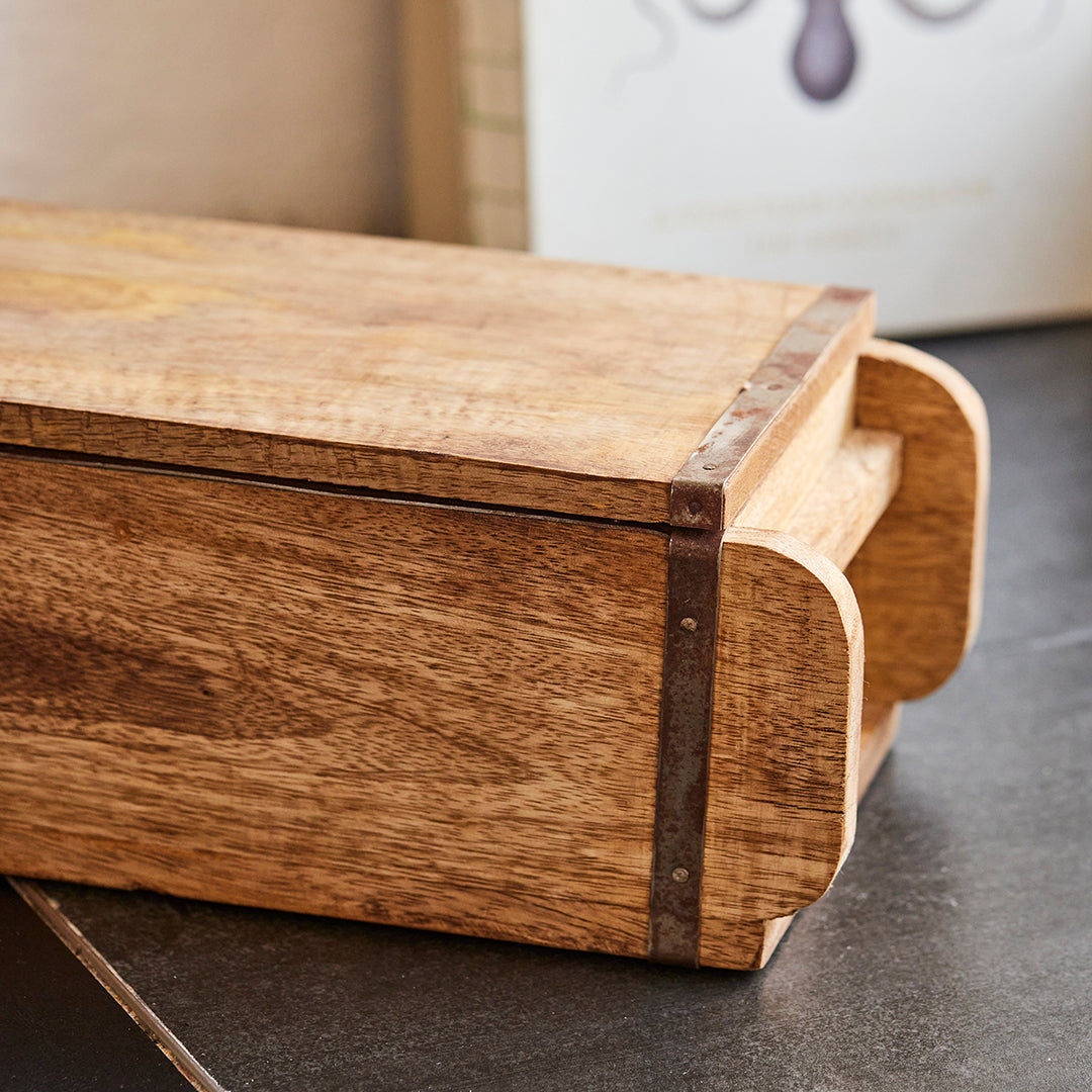 Boîte rectangulaire en bois avec renforts métalliques sur une surface foncée.