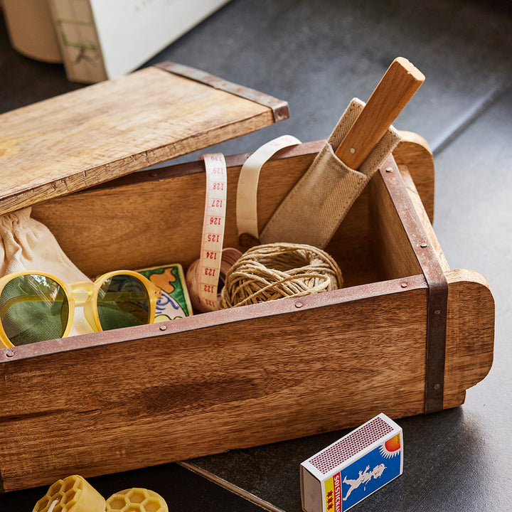 Coffret en bois contenant divers objets, dont des lunettes de soleil jaunes, un ruban à mesurer, une bobine de ficelle, une boîte d'allumettes et un outil à manche en bois.