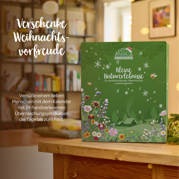 Un calendrier de l'Avent vert avec un motif floral se dresse sur une table en bois devant une étagère, avec le texte « Offrez le cadeau de l'anticipation de Noël » à côté.