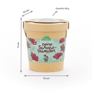Gobelet en papier avec motif floral et inscription « Deine Schokoblümchen », à côté des dimensions (10 cm de diamètre, 11 cm de hauteur) et du poids (60 g) indiqués en allemand.