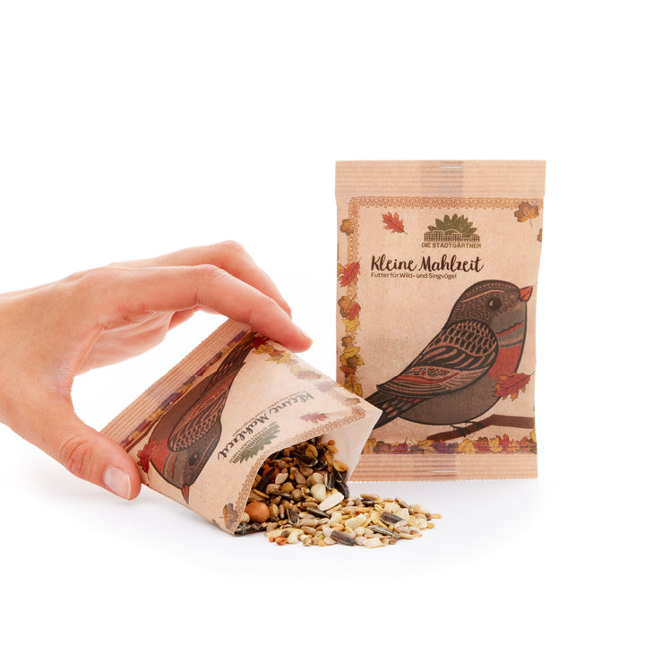 Verser à la main des graines pour oiseaux dans un sac en papier brun avec un motif d'oiseau et l'inscription « Small Meal » à côté d'un sac vertical non ouvert.