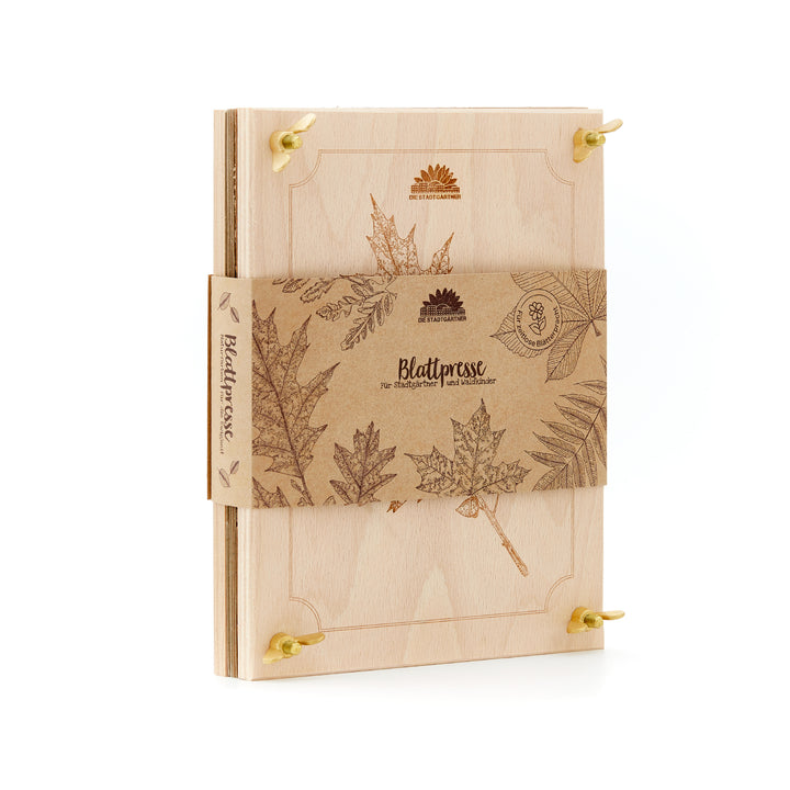 Presse à feuilles en bois avec gravures botaniques et bande de papier brun, sur laquelle sont imprimés des motifs de feuilles et l'inscription « Leaf Press ».