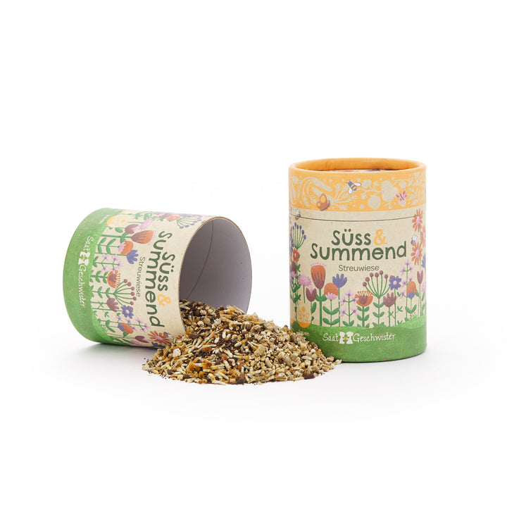 Deux boîtes en carton colorées aux motifs floraux, l'une debout et l'autre couchée, d'où tombent des graines de fleurs, étiquetées « Sweet & Buzzing Meadow ».