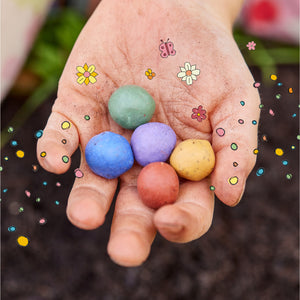 Une main tient cinq bombes de graines colorées, entourées de fleurs dessinées et de points colorés.