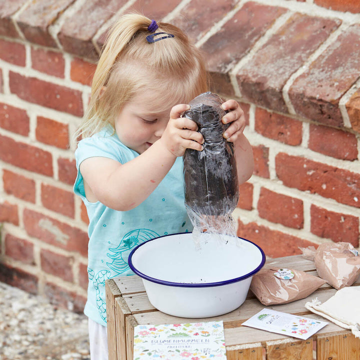 Petite fille versant de l'eau d'une bouteille dans un bol pendant qu'elle jardine.
