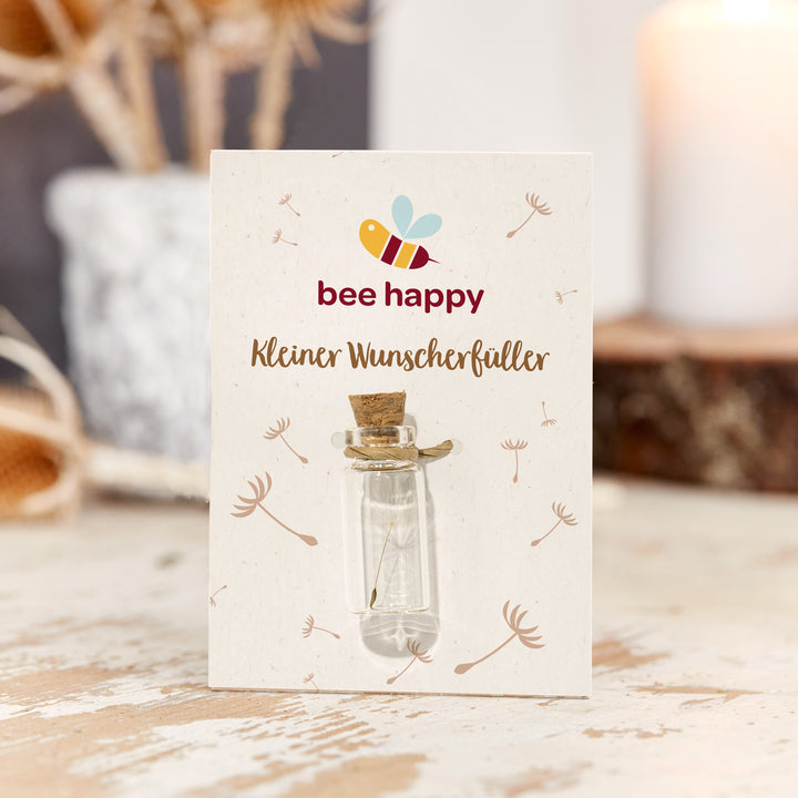 Petite bouteille en verre avec bouchon sur une carte avec l'inscription « abeille heureuse petite réalisatrice de souhaits », décorée de motifs de pissenlit.