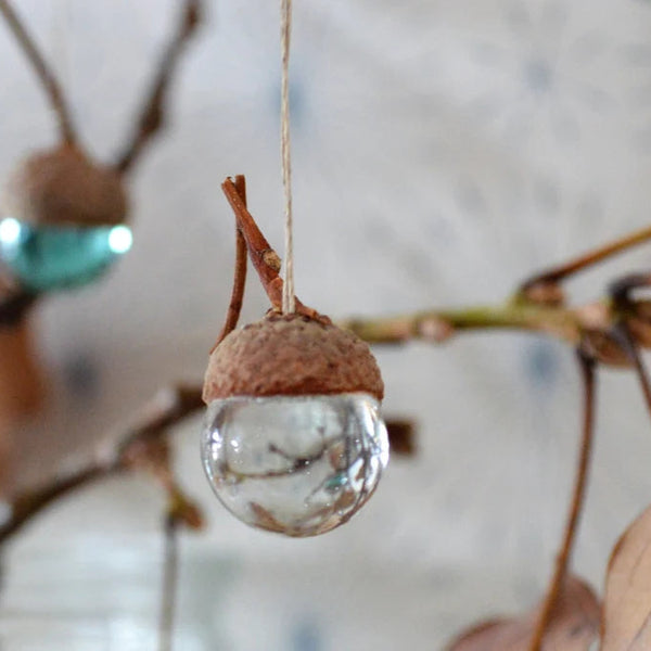 Un pendentif est suspendu à un bouquet automnal. Il est composé d'une tête de gland sur laquelle est collée une perle de verre.
