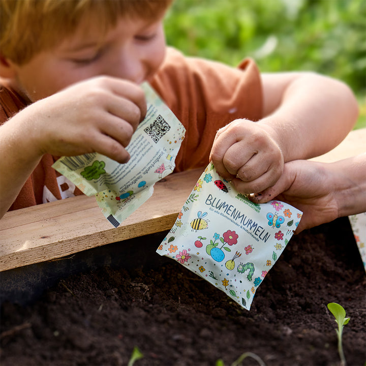 Un enfant tient un sac coloré étiqueté « bille de fleurs » au-dessus d’un lit de terre.
