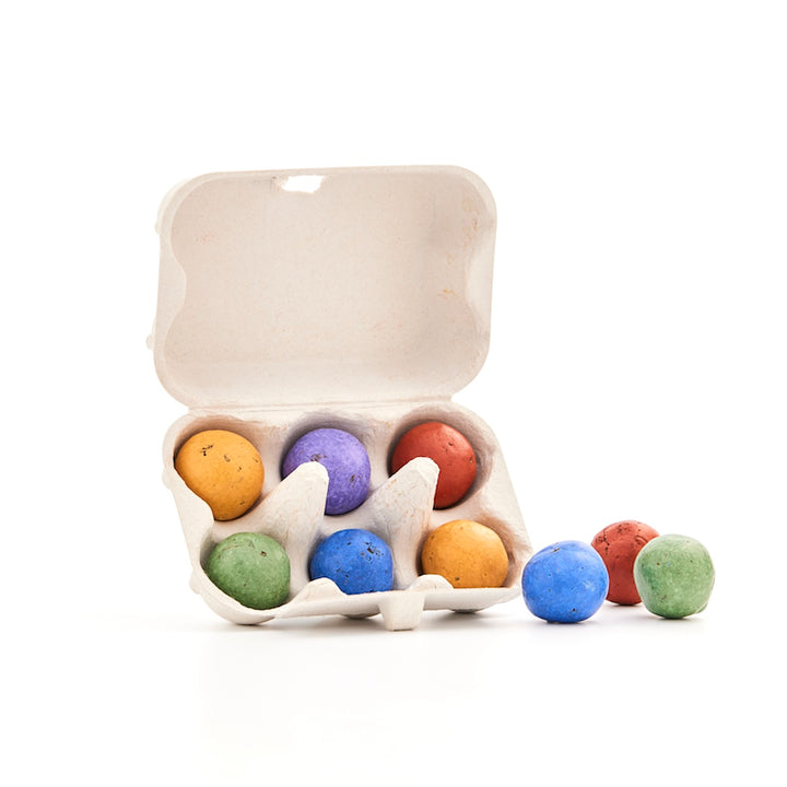 Une boîte à œufs ouverte avec six œufs de Pâques colorés et trois autres œufs colorés à côté d'eux sur un fond blanc.