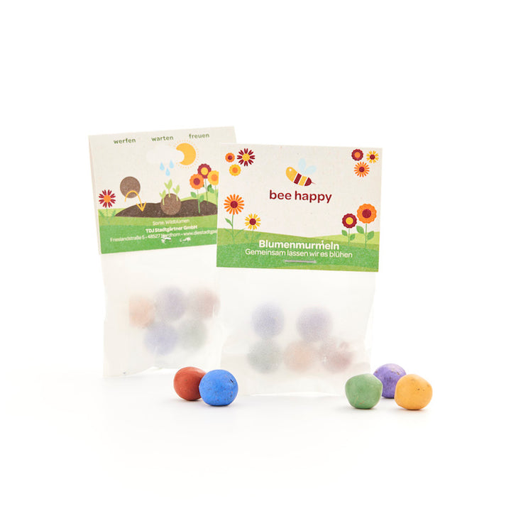 Deux petits sachets de billes colorées en forme de fleurs. L'emballage porte l'inscription « Bee Happy » et est illustré de fleurs et d'une abeille.