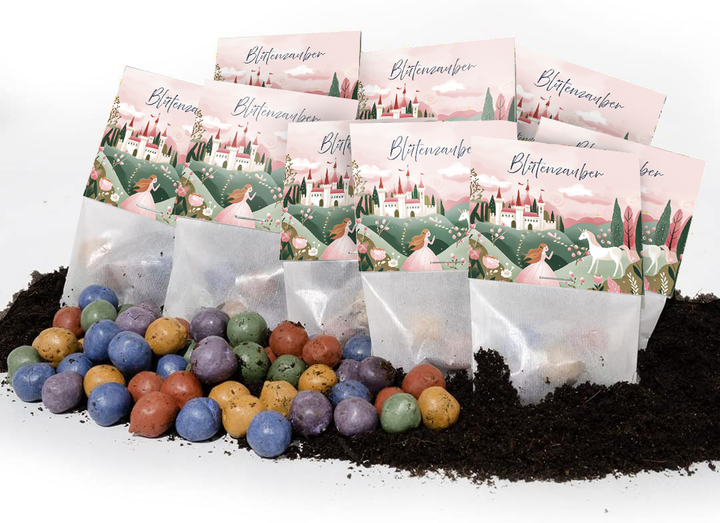 Plusieurs sacs étiquetés « Blütenzauber » (Magie des fleurs) avec un design de conte de fées, avec des bombes de graines colorées posées sur le sol devant eux.