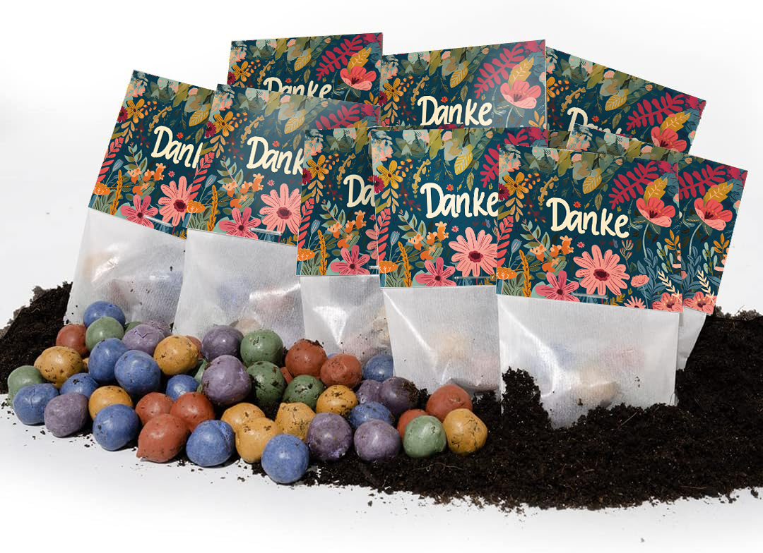 Plusieurs sacs colorés avec les mots « Merci » et des motifs floraux se trouvent sur le sol, avec des boules de graines colorées devant eux.
