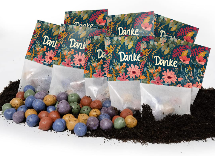 Plusieurs sacs colorés avec les mots « Merci » et des motifs floraux se trouvent sur le sol, avec des boules de graines colorées devant eux.