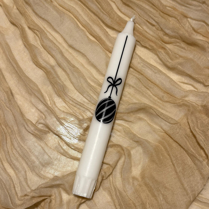 Une bougie blanche avec une boule de Noël noire comme motif repose sur une bordure en tissu doré
