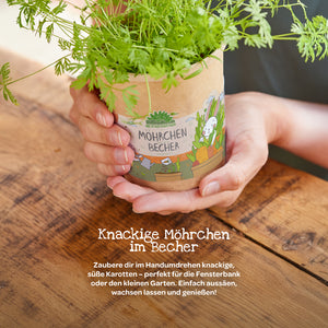 Personne tenant une tasse avec des plants de carottes en croissance sur une table en bois, étiquetée « Tasse de carottes ».