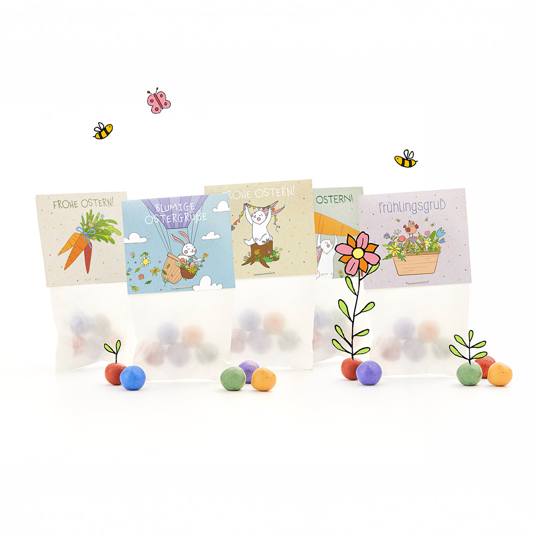 Quatre sacs de Pâques avec des boules colorées, chacun avec des motifs joyeux et illustrés de Pâques et de printemps et des salutations allemandes telles que « Joyeuses Pâques » et « Salutations de printemps », entourés de fleurs, d'abeilles et de papillons dessinés.