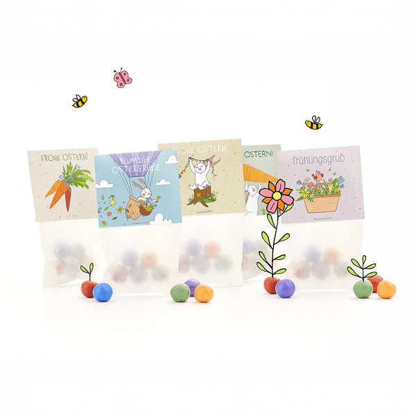 Quatre sacs de Pâques avec des boules colorées, chacun avec des motifs joyeux et illustrés de Pâques et de printemps et des salutations allemandes telles que « Joyeuses Pâques » et « Salutations de printemps », entourés de fleurs, d'abeilles et de papillons dessinés.
