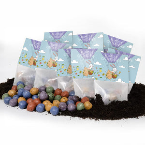Plusieurs petits sacs avec l'inscription "Flowery Easter Greetings" et un motif de lapin de Pâques, devant lesquels se trouvent des bombes de graines colorées sur de la terre.
