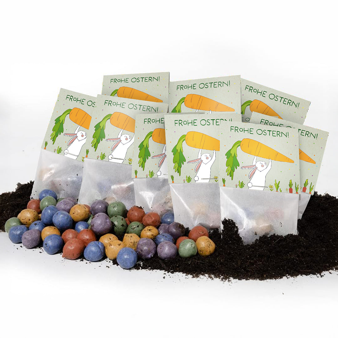 Plusieurs sachets de graines de Pâques avec l'inscription « Joyeuses Pâques ! » et des confettis de graines colorés sur la terre.
