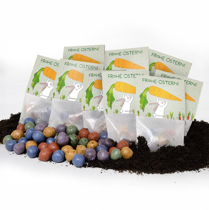 Plusieurs sachets de graines de Pâques avec l'inscription « Joyeuses Pâques ! » et des confettis de graines colorés sur la terre.