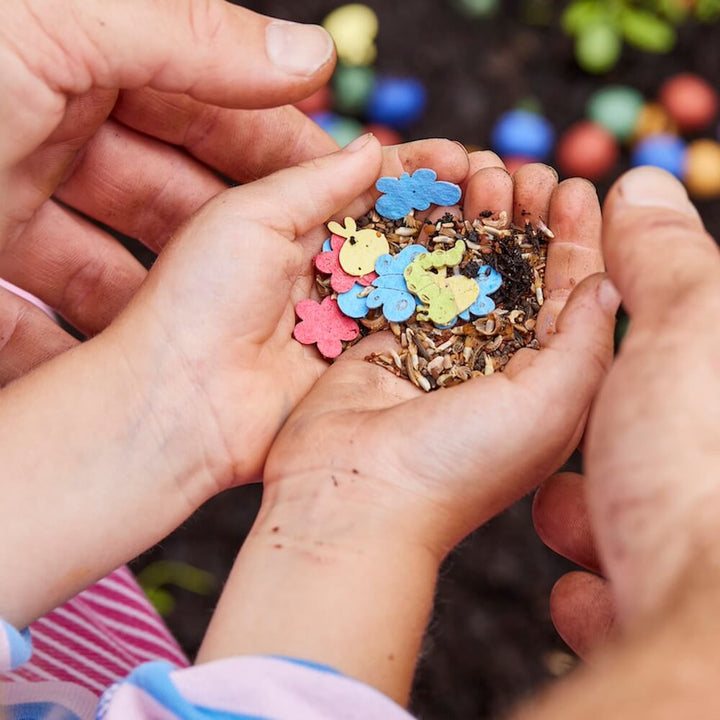 Les mains des enfants tiennent des graines colorées en forme d'animaux et de fleurs au-dessus du sol.