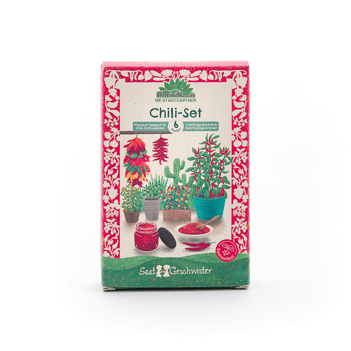 Emballage d'un ensemble de chili avec des illustrations colorées de plants de chili, de pots, de piments et d'un pot de poudre de chili, entourés d'un motif floral rouge.