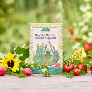 Un paquet de graines biologiques « Kinder-Garten » est posé sur une table en bois, entouré de tournesols, de radis, de tomates et de verdure fraîche dans le jardin.
