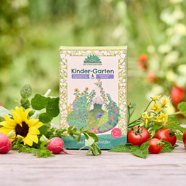 Un paquet de graines biologiques « Kinder-Garten » est posé sur une table en bois, entouré de tournesols, de radis, de tomates et de verdure fraîche dans le jardin.