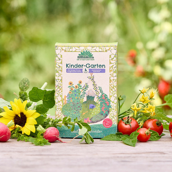 Un paquet de graines biologiques « Kinder-Garten » est posé sur une table en bois, entouré de tournesols, de radis, de tomates et de verdure fraîche dans le jardin.