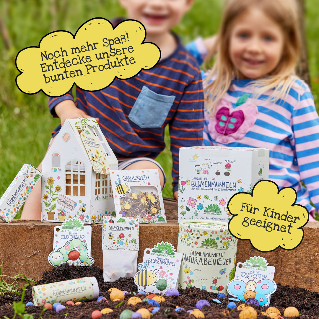 Deux enfants sont assis dans le jardin derrière une sélection de produits de graines de fleurs colorées et adaptées aux enfants ainsi que des emballages favorisant les aventures dans la nature et le jeu créatif.