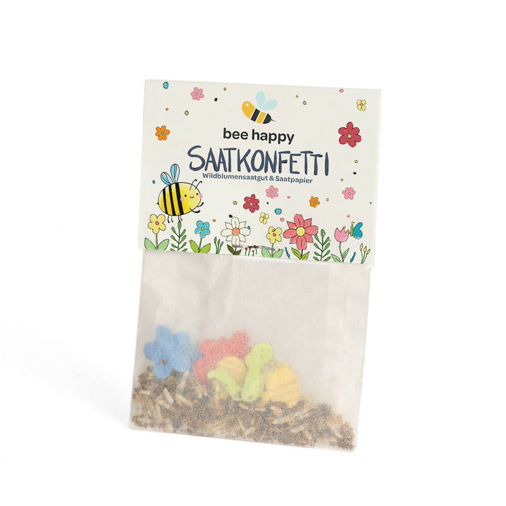 Sachet avec confettis de graines colorés et l'inscription "bee happy SEED CONFETTI graines de fleurs sauvages & papier de graines", décoré de motifs d'abeilles et de fleurs.