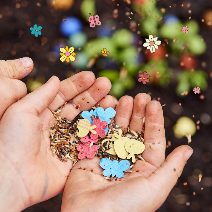 Deux mains d'enfants sales tiennent des graines de fleurs et des formes en papier colorées en forme de fleurs et de papillons au-dessus du sol.