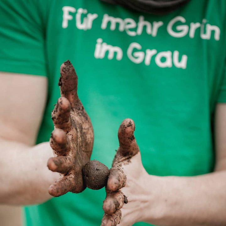 Une personne portant un t-shirt vert avec l'inscription « Pour plus de vert en gris » montre ses mains sales avec de la terre.