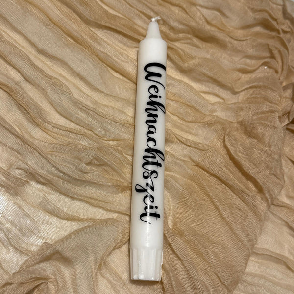 Bougie blanche avec l'inscription noire « Christmas time » sur le côté drapée sur un tissu doré