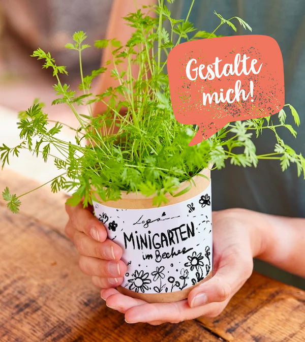 Personne tenant une tasse avec une plante aromatique sur laquelle est écrit « Mini jardin dans une tasse » et « Concevez-moi ! »