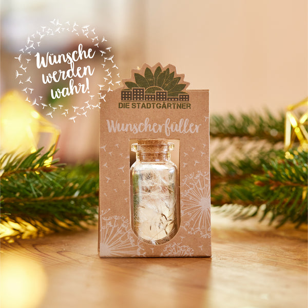 Une petite bouteille en verre avec un bouchon sur un emballage étiqueté « The City Gardeners Wish Fulfillers » à côté de branches de sapin et de décorations de Noël.