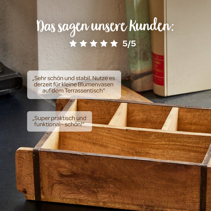 Une boîte en bois avec des compartiments se trouve sur une table, avec des livres en arrière-plan ; au-dessus se trouvent des avis clients en allemand et cinq étoiles avec une note de 5/5.