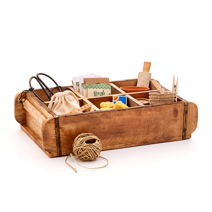 Coffret en bois contenant divers ustensiles de jardinage tels que des ciseaux, des sacs de graines, des pots de fleurs, de la ficelle et d'autres accessoires.