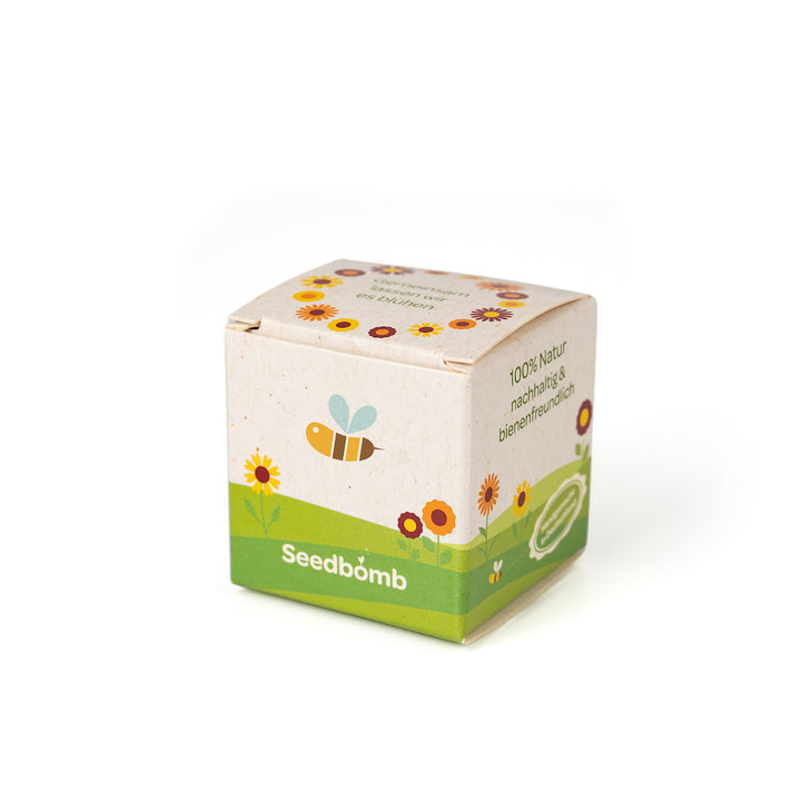 Petite boîte étiquetée « Seedbomb » entourée d'illustrations florales, avec des références au fait qu'elle est 100 % naturelle et respectueuse des abeilles.