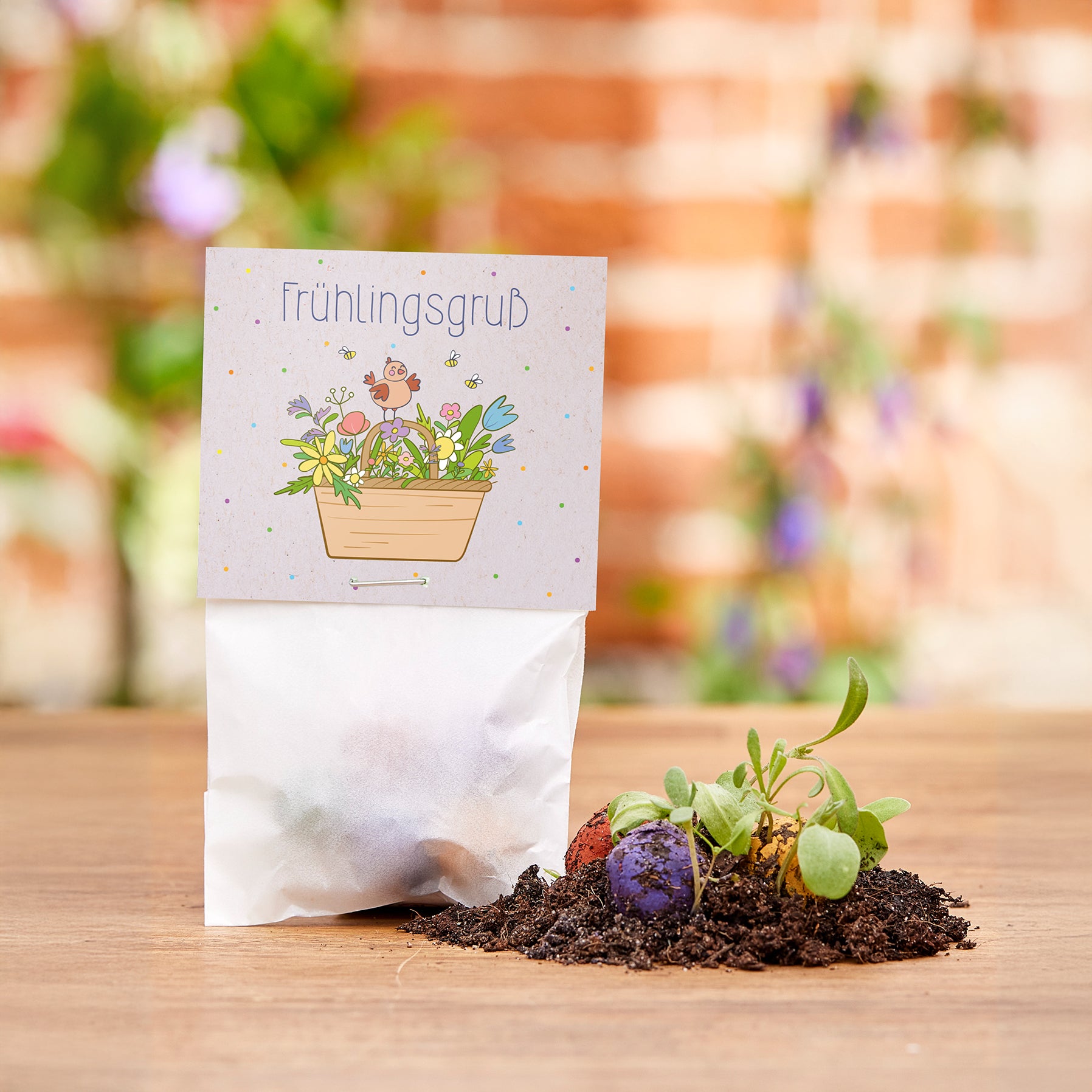 Un petit sac étiqueté « Salutations de printemps » se trouve sur une table en bois, avec de la terre, des bombes de graines colorées et de jeunes plantes à côté.