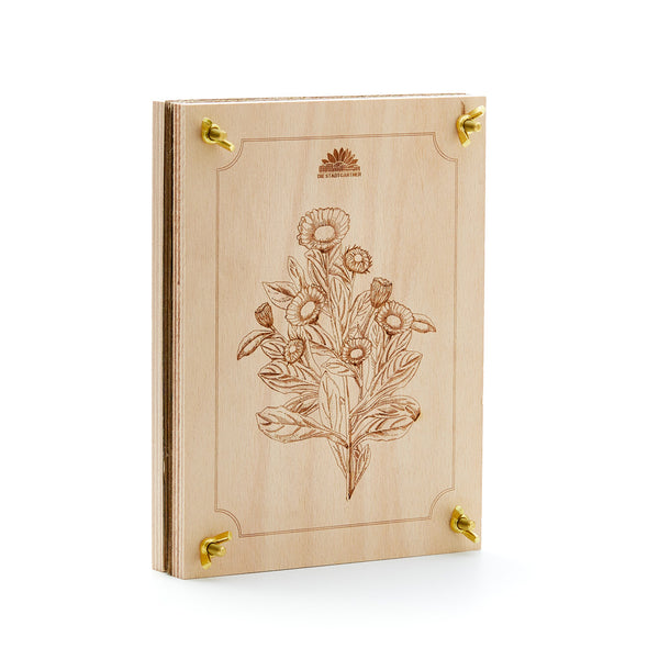 Livre en bois avec motif de gravure florale et coins en métal doré, posé sur un fond blanc.