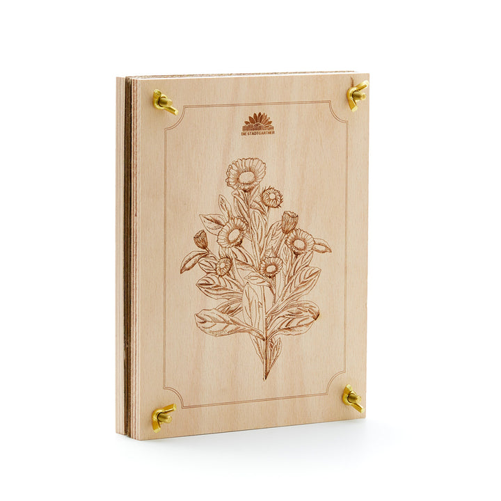 Livre en bois avec motif de gravure florale et coins en métal doré, posé sur un fond blanc.