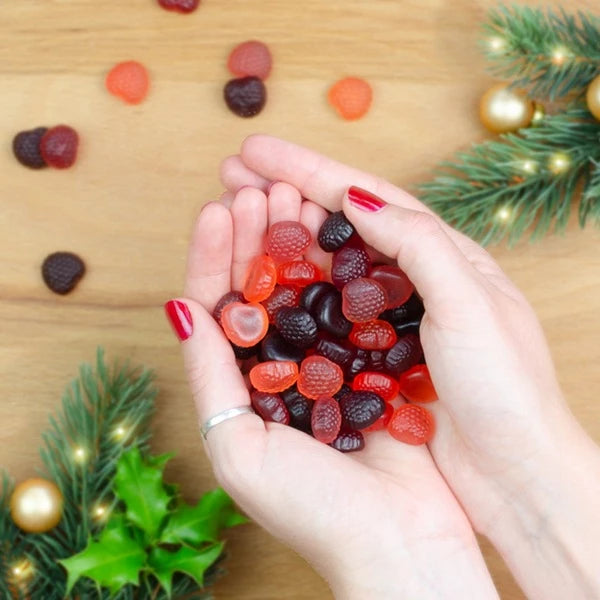 Mains avec du vernis à ongles rouge tenant des oursons en gélatine, décorations d'hiver en arrière-plan.
