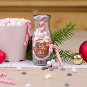 Bouteille étiquetée « Chocolat chaud » à côté de décorations de Noël et d'une tasse de guimauves.