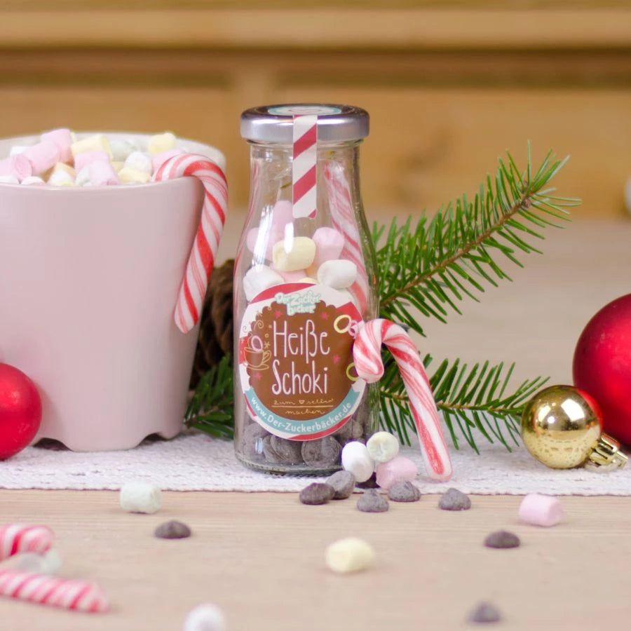 Bouteille étiquetée « Chocolat chaud » à côté de décorations de Noël et d'une tasse de guimauves.