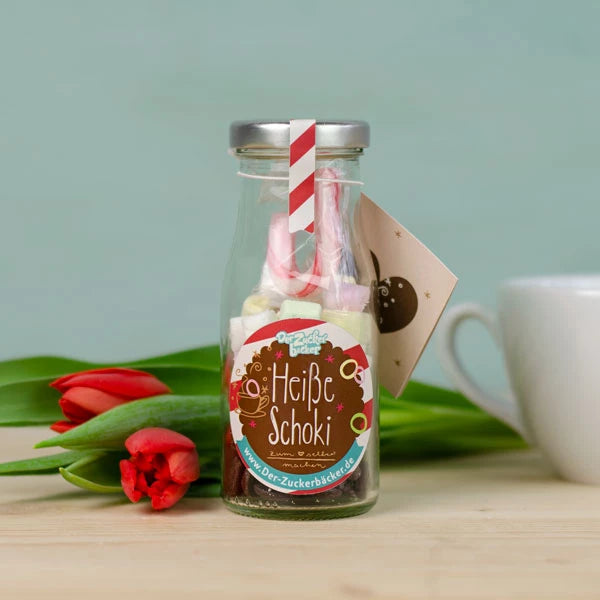 Bouteille avec étiquette « Chocolat chaud » et paille, à côté d'une tulipe rouge et d'une tasse en arrière-plan.