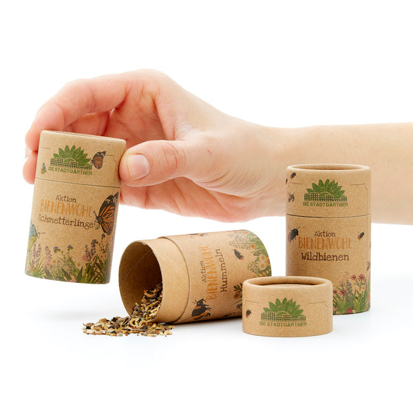 La main ouvre un tube en carton avec l'inscription « Aktion BIENENWEHL » et des graines pour abeilles sauvages et papillons.