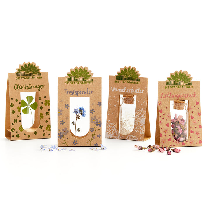 Quatre coffrets cadeaux de « Die Stadtgärtner » avec des petits pots et diverses plantes séchées, ainsi que des étiquettes : Porte-bonheur, Consolateur, Exauceur de vœux et Personne préférée.
